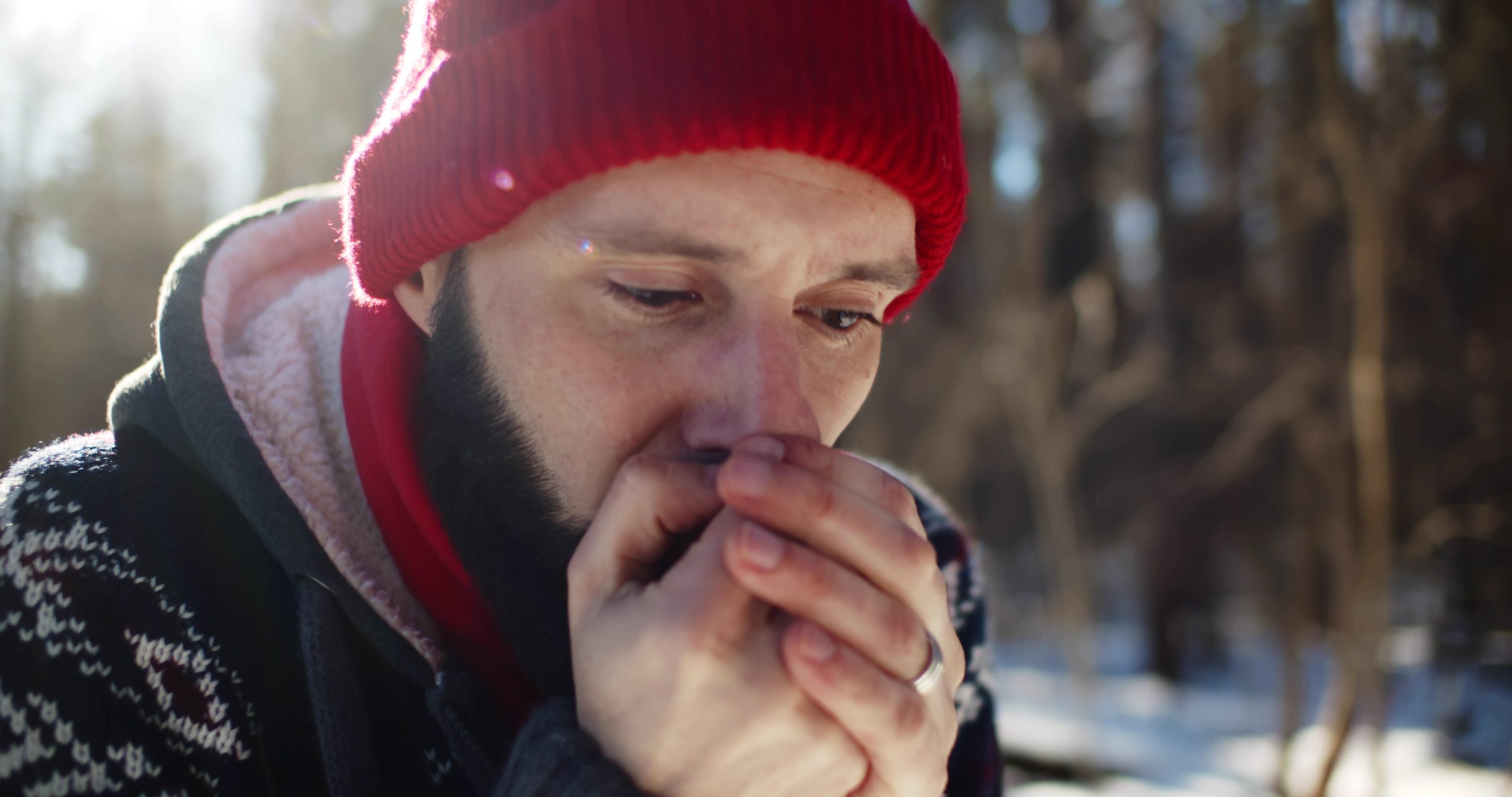 Hiker blowing on bare, cold hands to warm them in a snowy winter forest