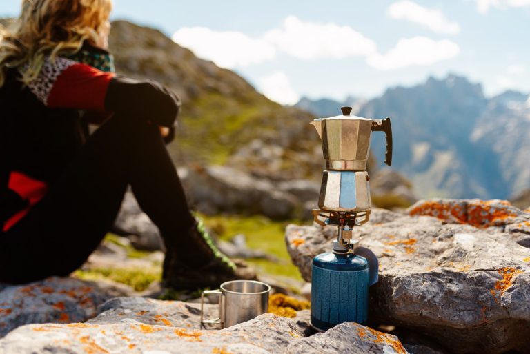 Woman preparing coffee on a camping stove in the mountains at a backcountry camp