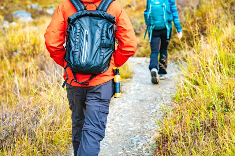 A hiker walking an autumn alpine trail with a can of bear spray in a holster on the right hip, a second hiker ahead