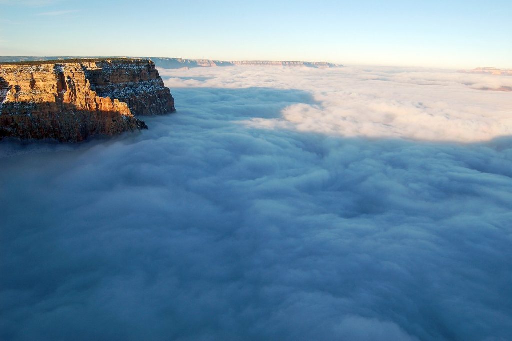 A sunlit cliff of the Grand Canyon rim standing above a level sea of cloud that fills the canyon to the horizon