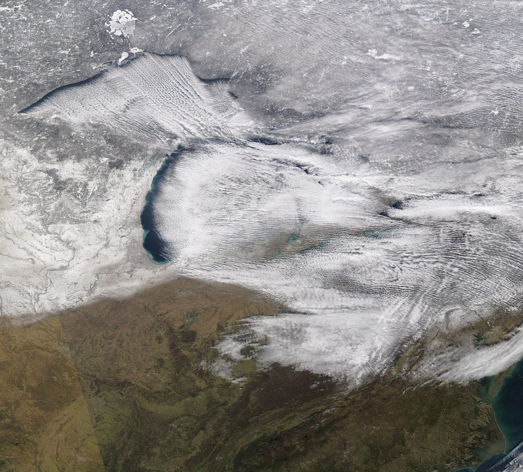 Satellite view of the Great Lakes in winter with parallel streaks of white cloud streaming off each lake onto the land downwind